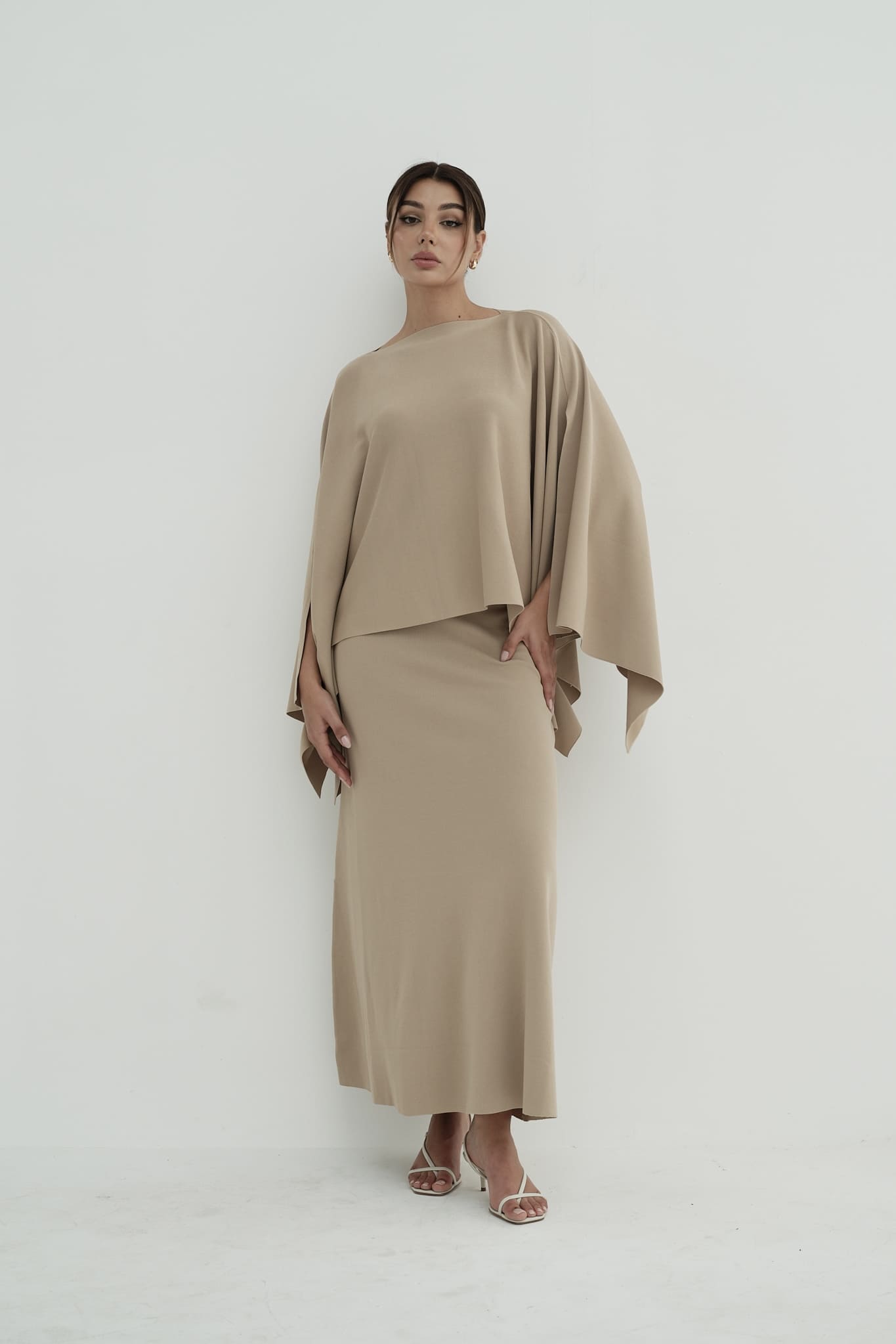 Model wearing Amanda Set featuring a draped cape top and a matching floor-length skirt, styled with white strappy sandals, standing against a white background