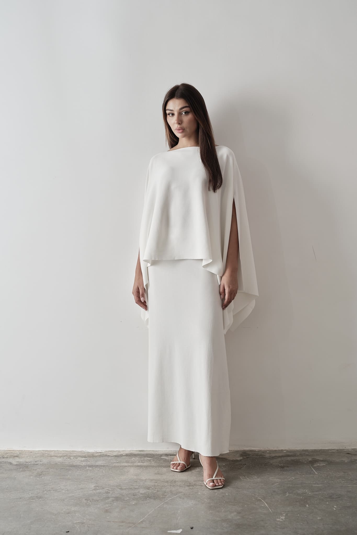 Model wearing Amanda Set featuring a draped cape top and a matching floor-length skirt, styled with white strappy sandals, standing against a white background