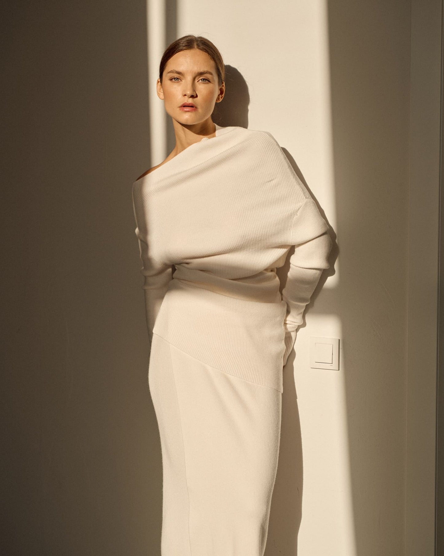 Avani Set in a creamy off-white ribbed knit fabric. The outfit features a long-sleeve asymmetrical draped top paired with a sleek matching skirt, minimalist, elegant aesthetic.
