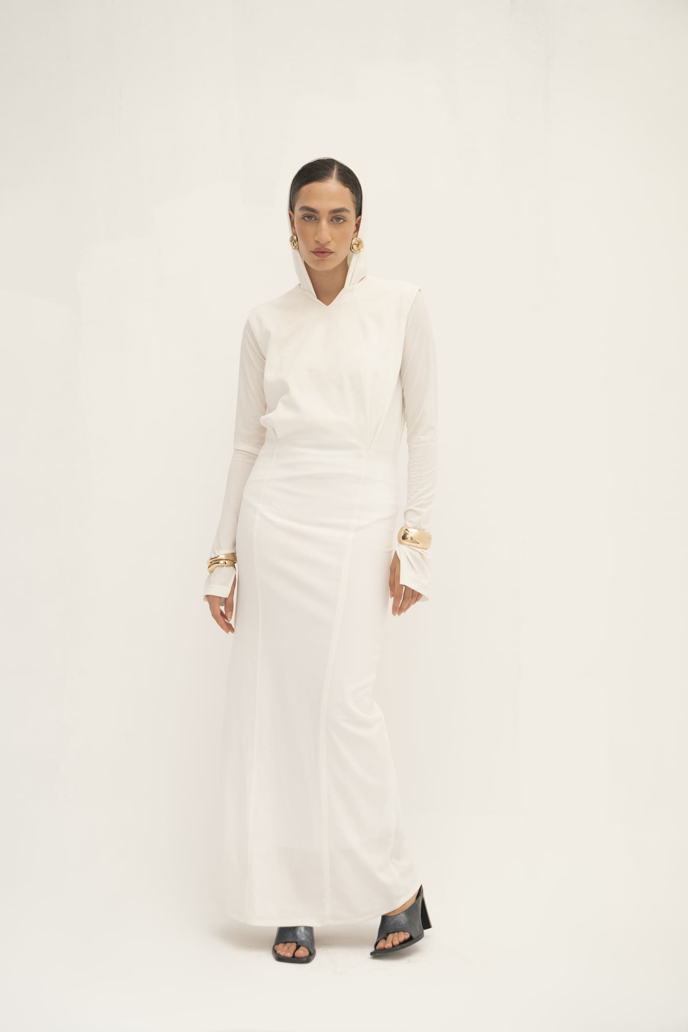 A woman stands against a plain white background, dressed in the elegant Avelia & Elyse Set featuring flared sleeves and accessorized with gold bracelets. Her dark hair is pulled back, and she complements her outfit with black open-toe heels, capturing a contemporary aesthetic that is both stylish and poised.