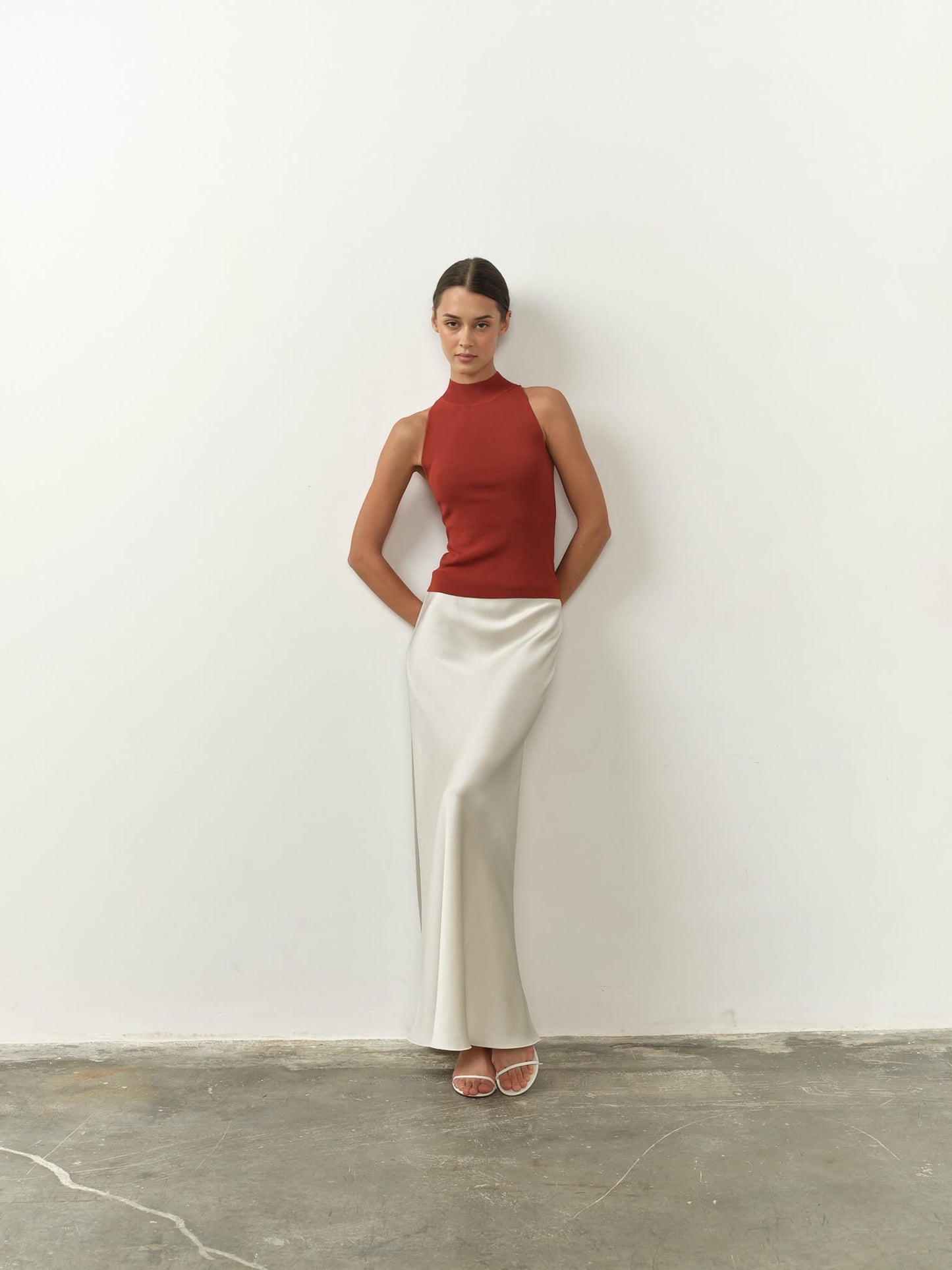 Sleek sleeveless burnt orange top featuring a high neck, fitted silhouette, and lightweight fabric, paired with a satin skirt for a chic and minimalist aesthetic.