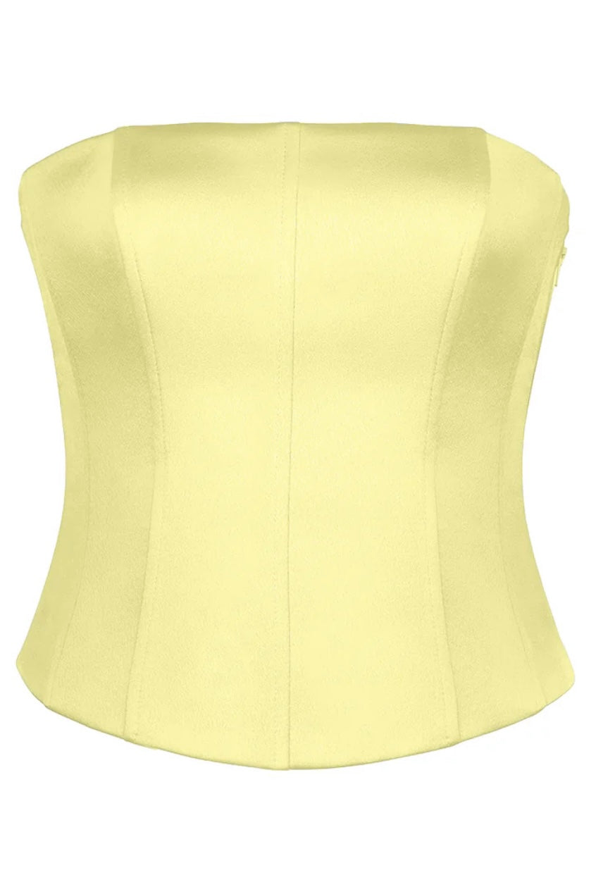 The Regina Corset Top, in a luxurious yellow shade, is made from sculpting satin fabric. This strapless design includes front seams for a structured fit and a gently curved neckline, evoking the style of a Bridgerton corset. The sleek fabric provides an elegant finish with no visible decorations or patterns.